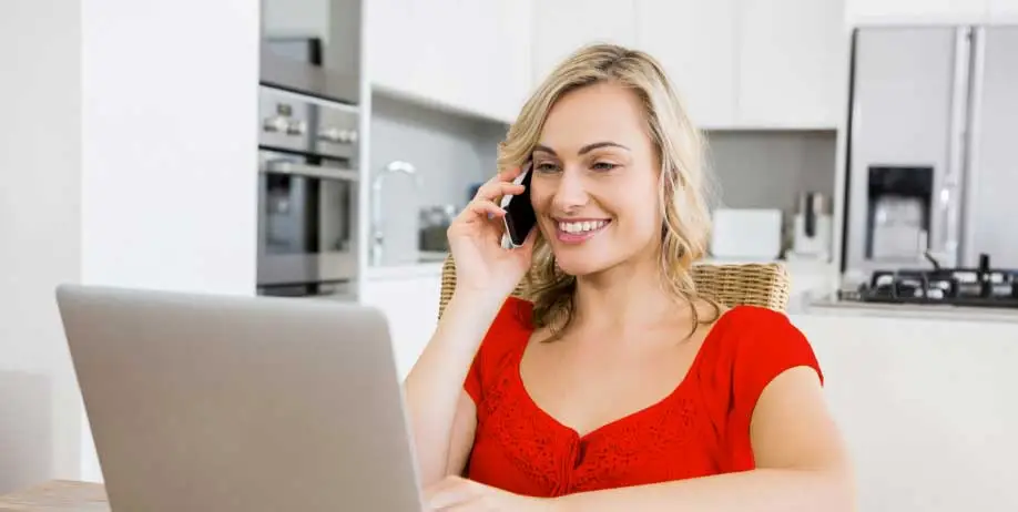 GYMGUYZ In-Home Personal Training A woman on her phone looking at her computer.